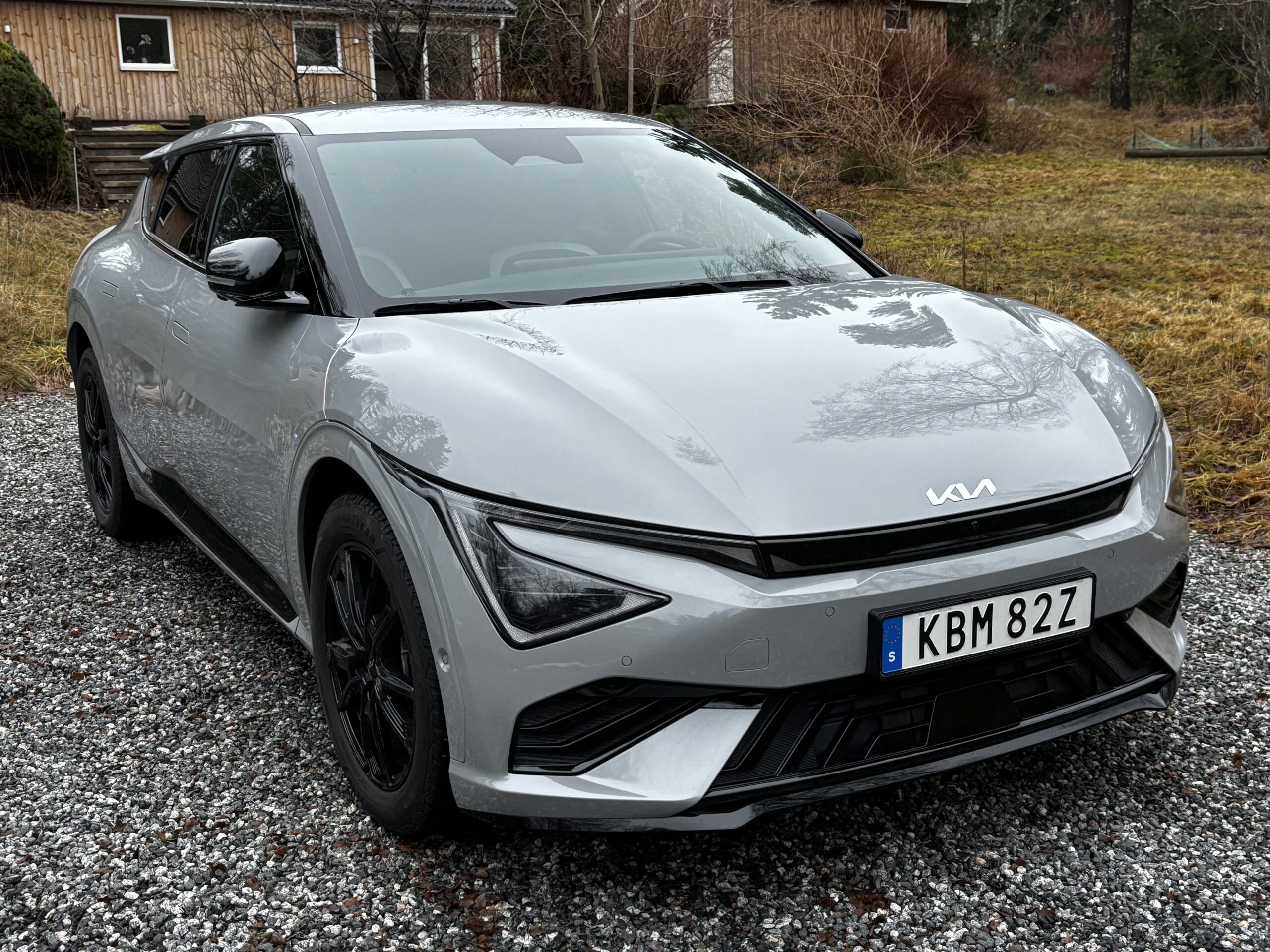 Kia EV6 Long Range. Exteriör snett framifrån. Bilen står på en grusplan med hus och grönområde i bakgrunden.